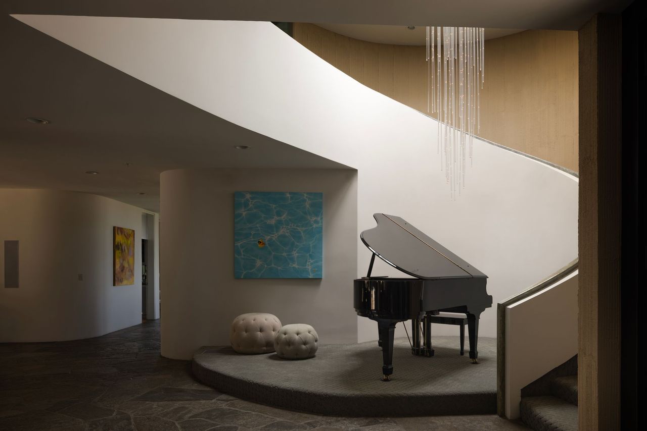 Foyer with grand piano beneath a sculptural curved staircase